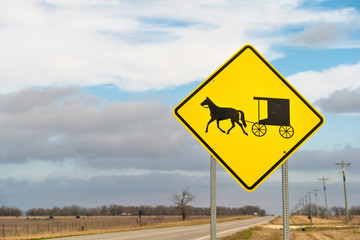 Yellow Road Sign warning traffic of horse and buggy on rural country highway roadside on a mostly cloudy day.