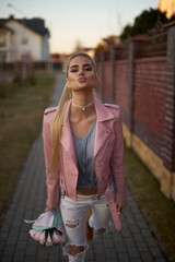 Beautiful cute blonde girl with bouquet of delicate pink tulip flowers at sunset in cool pink jacket