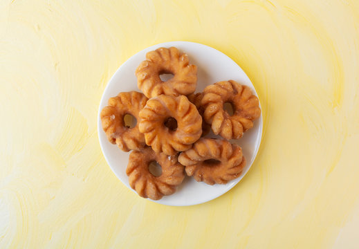 Glazed crullers on a plate atop a yellow background