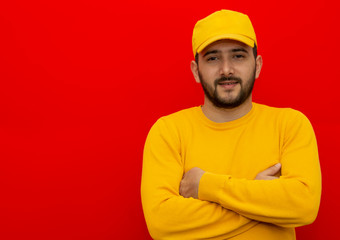 Young guy delivery man, loader, worker in a yellow cap and shirt in an isolated red background. place for text