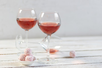Couple of standing and one laying glasses  with rose wine, round sweets on white wooden background