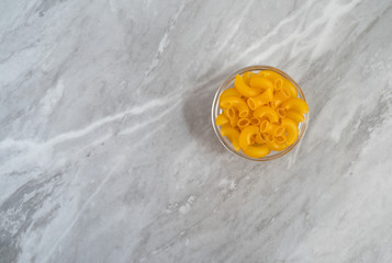 Organic elbow macaroni in a glass bowl offset on a gray countertop