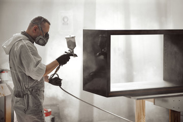 Man Painting Furniture Details.  Painter with safety mask painting a wooden furniture with spray gun.