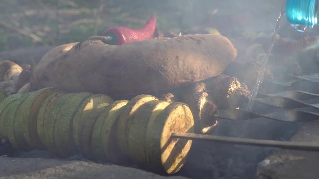 pita bread and chili pepper on kebab, vegetables and meat, zucchini and onions, guy pours water into the fire, cooks kebab