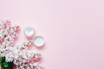 Natural cosmetics product with lilac flowers and jar creme on a pink background. Spa, skin care, body treatment. Top  view and copy space flat lay.