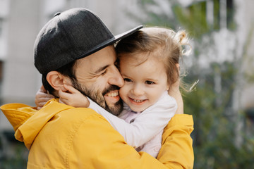 Fototapeta premium Portrait of a stylish pretty Father and his little daughter, they went for a walk on the playground in the courtyard of a multi-storey building