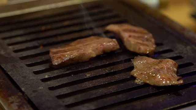 Slow-motion of thinly sliced Japanese tongue wagyu beef on grille for barbecue. Grill one of the best beef in Japan. Style Yakiniku meaning grilled meat cuisine. BBQ food.-Dan