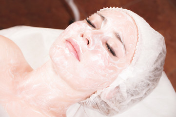 A young attractive girl in a cosmetologist s office with her face covered in a cosmetic rejuvenating white mask with a brush applied lies and relaxes. Facial skin care concept