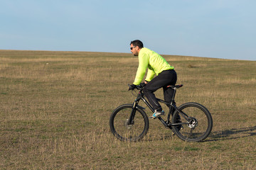 Fototapeta premium Cyclist in pants and green jacket on a modern carbon hardtail bike with an air suspension fork. The guy on the top of the hill rides a bike.