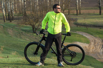 Cyclist in pants and green jacket on a modern carbon hardtail bike with an air suspension fork. The guy on the top of the hill rides a bike.