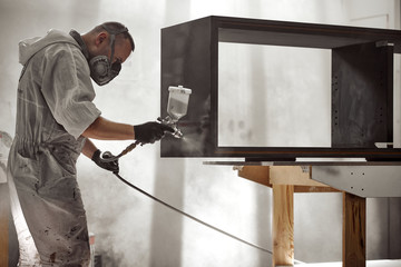 Man Painting Furniture Details.  Painter with safety mask painting a wooden furniture with spray...
