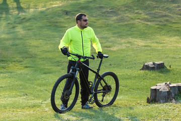 Obraz premium Cyclist in pants and green jacket on a modern carbon hardtail bike with an air suspension fork. The guy on the top of the hill rides a bike.