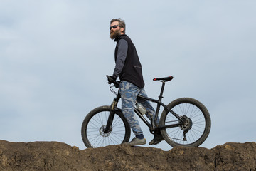 Fototapeta premium Sports brutal bearded guy on a modern mountain bike. Beautiful view from the mountain. Panoramic view for banner.