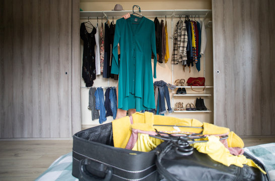 woman packing a suitcase trying on clothes wardrobe in background