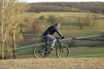 Sports brutal bearded guy on a modern mountain bike. Cyclist on the green hills in the spring.