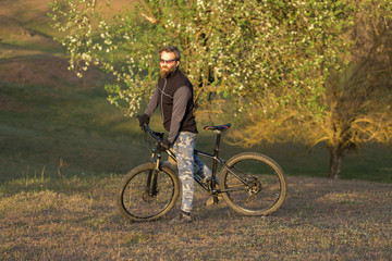Obraz premium Sports brutal bearded guy on a modern mountain bike. Cyclist on the green hills in the spring.
