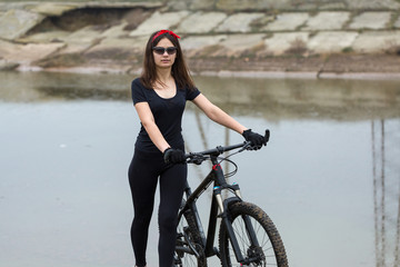 Fototapeta premium Girl on a mountain bike on offroad, beautiful portrait of a cyclist in rainy weather, Fitness girl rides a modern carbon fiber mountain bike in sportswear. Close-up portrait of a girl in red bandana.