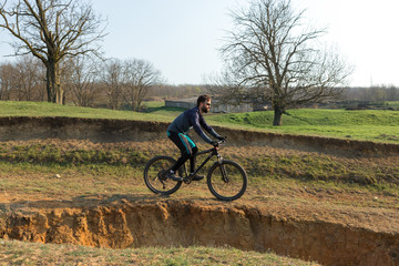 Obraz premium Cyclist in shorts and jersey on a modern carbon hardtail bike with an air suspension fork standing on a cliff against the background of fresh green spring forest