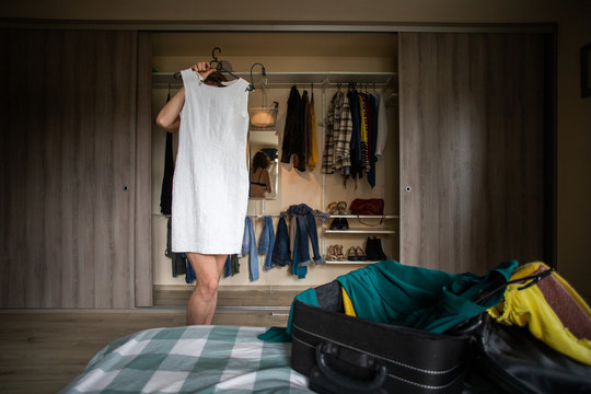 woman packing a suitcase trying on clothes wardrobe in background