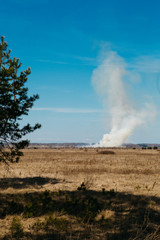 A tall column of white smoke in a dry field in spring. Fire hazard in the spring setting fire to dry grass