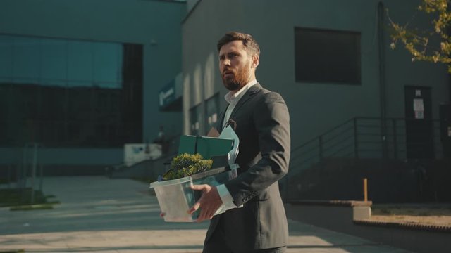 Sad office worker man walking with box of personal stuff lose a job got fired due to a coronavirus crisis unemployed depression business corporate employment economy slow motion