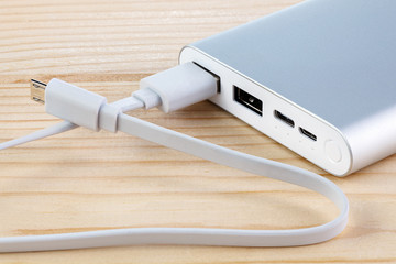 An additional stand-alone power bank for charging mobile devices. External battery on a wooden background. White charger for smartphone (battery bank). Full depth of field.