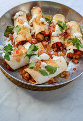 Mexican enchiladas topped with cheese, yoghurt sauce and coriander garnish. Vegetarian enchiladas made with lentils and red peppers. Mexican fast food. 