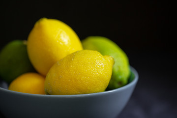 A lot of citrus fruits in a blue bowl on the dark background. Fresh lemons in a bowl. Close up of...