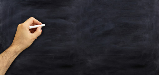 Left hand with a chalk against blackboard, copy space