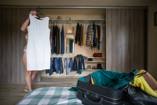 woman packing a suitcase trying on clothes wardrobe in background