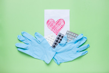 Greeting card with a painted red heart, blisters with pills and rubber protective gloves. Medicine. Layout. Green background