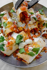 Mexican enchiladas topped with cheese, yoghurt sauce and coriander garnish. Vegetarian enchiladas made with lentils and red peppers. Mexican fast food. 
