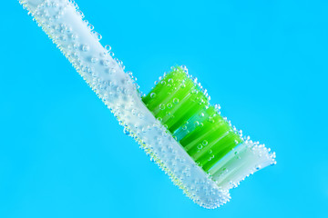 Manual toothbrush with green bristles in bubbles of air on blue background. Fresh breath concept.