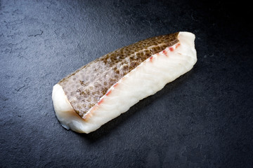 Raw Norwegian skrei cod fish filet with skin as closeup on black board with copy space