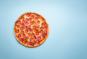 Pepperoni pizza top view on a blue background.