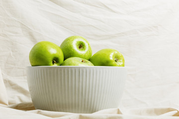 Green apples in a bowl on a light fabric background. Harvest apples, summer season, fresh fruits.