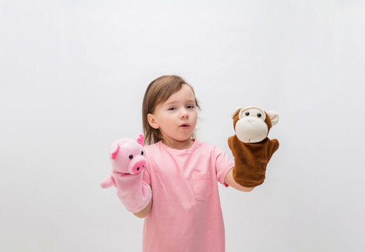 A little girl on a white background plays a puppet theater. Cute girl holding a toy monkey and pig. A little girl with loose hair in a pink t-shirt.
