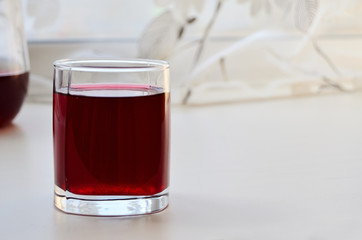 glass with currant juice on a white window sill with curtains