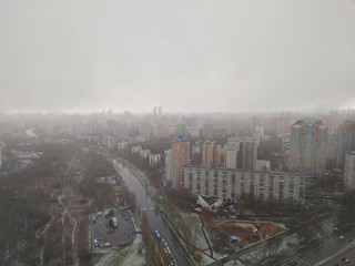 Fototapeta na wymiar Aerial photo of a big city with multi-storey residential buildings from a height in cloudy weather with snowfall, dark clouds and a distant horizon
