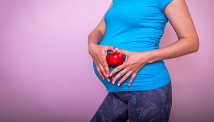 Pregnancy, healthy food and people concept - close up of happy pregnant woman eating red apple at home