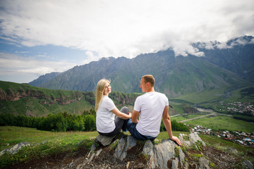 Naklejka premium young beautiful couple travelers girl blonde in a white t-shirt, a man in a white t-shirt stand on a background of mountains in Georgia