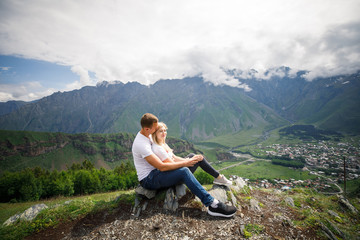 young beautiful couple travelers girl blonde in a white t-shirt, a man in a white t-shirt stand on a background of mountains in Georgia