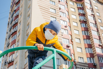 Fototapeta premium A small boy in a mask walks on the Playground during the quarantine. Stay at home
