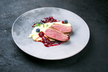 Traditionelles Gourmet Entenbrust Filet mit Kartoffel Püree und Preiselbeeren Sauce als closeup auf einem Modern Design Teller