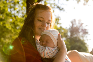 A young mother with a small newborn in her arms in a summer park. Happiness Maternity, Recovery Postpartum Concept