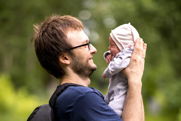 A young father with a small newborn in his arms walks in a summer park