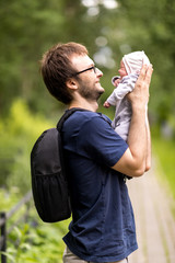 A young father with a small newborn in his arms walks in a summer park