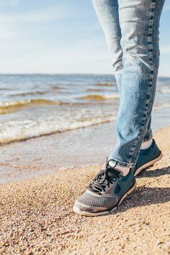 Long slim legs of a girl in jeans and sneakers for a walk along the seashore - a fresh sea breeze