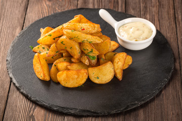 Fried potato wedges on a round black board with mustard sauce.