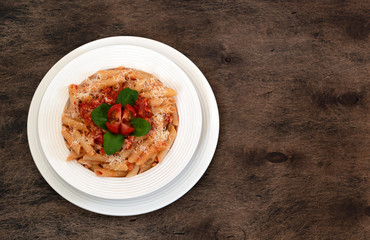 Penne rigate pasta with bolognese sauce in a white bowl on a dark wooden background